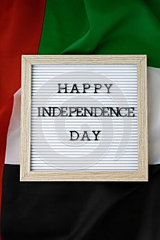 Text HAPPY INDEPENDENCE DAY on background waving flag of UAE. National holiday of United Arab Emirates. Commemoration