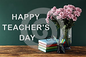 Text Happy Teacher`s Day on green chalkboard near table with stationery and bouquet