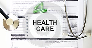 Text Health Care in a notebook on medical forms with a phonendoscope and green pills
