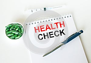 Text Health Check written in a notebook with a blue pen and a bunch of pills