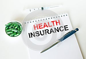 Text Health Insurance written in a notebook with a blue pen and a bunch of pills