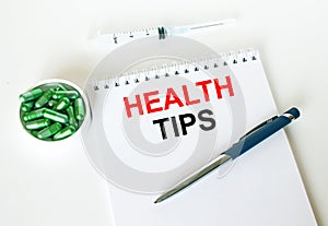 Text Health Tips written in a notebook with a blue pen and a bunch of pills