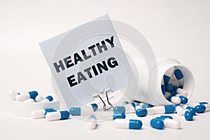 Text - HEALTHY EATING, written on sticky note near blue-white pills spilling out of pill bottle. Medical concept