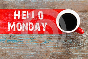 Text HELLO MONDAY and cup of aromatic coffee on wooden background, closeup