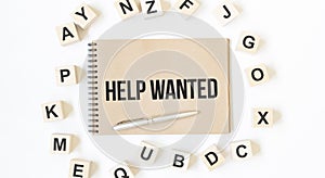 Text Help Wanted on the craft colored notepad with block wood cubes on the white background