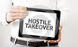 Text HOSTILE TAKEOVER on tablet display in businessman hands on the white background. Business concept