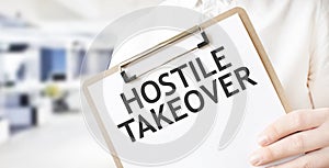 Text HOSTILE TAKEOVER on white paper plate in businessman hands in office. Business concept