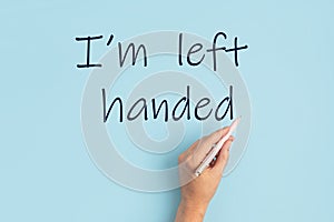 Text I am left handed and left hand with pen over blue background. International left handers day idea