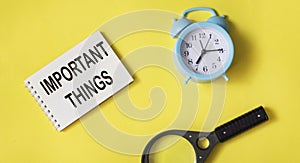 Text Important things on a notepad on a yellow background with a magnifying glass and a clock