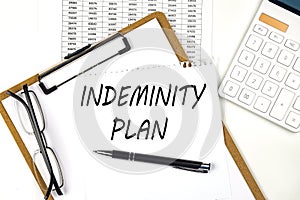 Text INDEMNITY PLAN on the white paper on clipboard with chart and calculator
