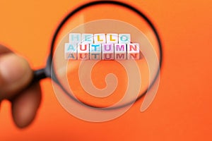 Text or inscription hello autumn. Cubes with letters under a magnifying glass on an orange background with copyspace