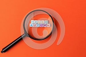 Text or inscription hello autumn. Cubes with letters under a magnifying glass on an orange background with copyspace