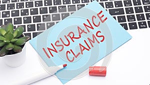 text INSURANCE CLAIMS is written in red marker on a blue card. in the frame is a laptop keyboard and a green cactus on a
