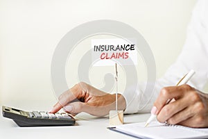 The text insurance claims written on a white paper card clamped in a paper holder. in the background woman`s hands writing with