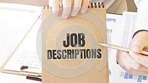 Text Job Descriptions on brown paper notepad in businessman hands on the table with diagram. Business concept