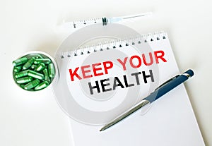 Text Keep Your Health written in a notebook with a blue pen and a bunch of pills