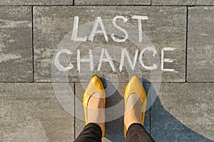 Text last chance written on gray sidewalk with women legs, top view