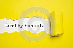The text Lead by example appearing behind torn brown paper