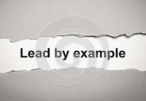The text lead by example appearing behind torn grey paper