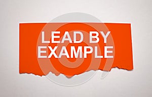 The text lead by example appearing behind torn grey paper