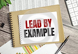 Text lead by example on notepad and pen on wooden background