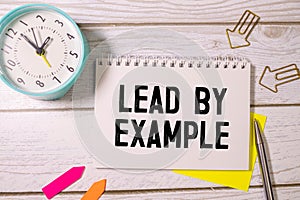 Text LEAD BY EXAMPLE on white paper on clipboard with chart and calculator
