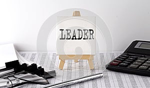 Text LEADER on easel with office tools and paper.Top view. Business concept