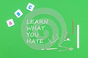 Text learn what you hate, from above wooden minitures school supplies and abc letters on green background