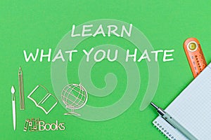 Text learn what you hate, school supplies wooden miniatures, notebook on green background