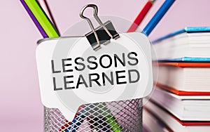 Text LESSONS LEARNED a white sticker with office stationery background. Flat lay on business, finance and development concept