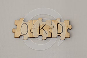 Text lettering OCD handwritten on wooden puzzles. Assembled abbreviation on blue background.