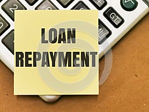 Text LOAN REPAYMENT written on yellow paper note on calculator. photo