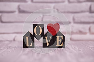 Text love on black wooden blocks with red heart on white brick background.