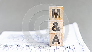 text MA - Mergers and Acquisitions - acronym concept on cubes and diagrams on a gray background, business as usual