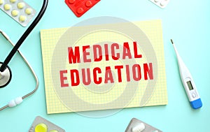 The text MEDICAL EDUCATION is written in a yellow notebook that lies next to the stethoscope. Blue background.