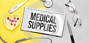 Text medical supplies on notebook with stethoscope,glasses, pen,thermometer, red pills and pen on yellow background. Medical