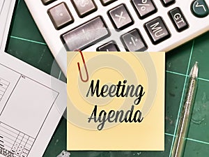 text Meeting Agenda written on yellow paper note with a pen and calculator. photo