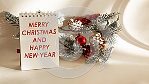 Text MERRY CHRISTMAS AND HAPPY NEW YEAR on a notebook with Christmas tree decorations on a white background .