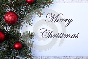 Text merry christmas on paper with fur-tree, branches, colored glass balls , decoration and cones on a wooden background