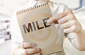 Text MILE on brown paper notepad in businessman hands in office. Business concept