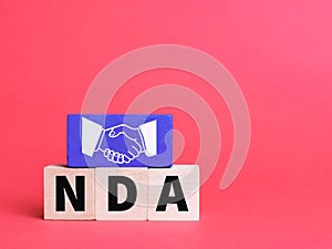 Text NDA on wooden cubes against red background with hand shake icon.