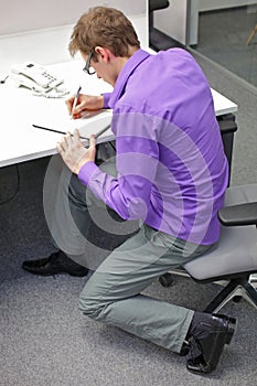 Text neck - man in slouching position  writing on paper with pen at desk