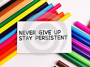 Text NEVER GIVE UP STAY PERSISTENT on paper note with colorful pencils isolated on white background.