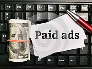 Text PAID ADS written on white paper note with pen and fake money on computer keyboard. photo