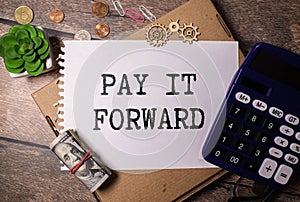 Text PAY IT FORWARD on a notebook with office tools on white background