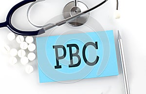 Text PBC on a table with a stethoscope,pills and pen, medical concept