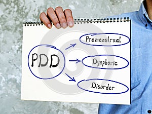 Text PDD Premenstrual Dysphoric Disorder on Concept photo. man`s hand holding hardcover kraft notebook