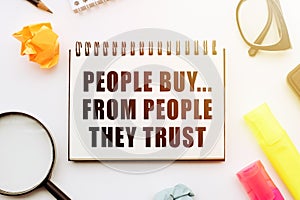 Text - People Buy From People They Trust in notebook on white table with office tools