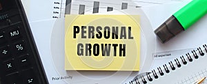 Text PERSONAL GROWTH on the page of a notepad lying on financial charts on the office desk