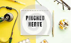 Text PINCHED NERVE on notebook with stethoscope and pen on yellow background.